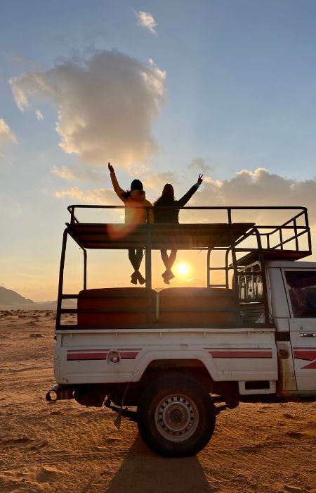 Voyageuses sur le toit d'une jeep au coucher du soleil dans le Wadi Rum